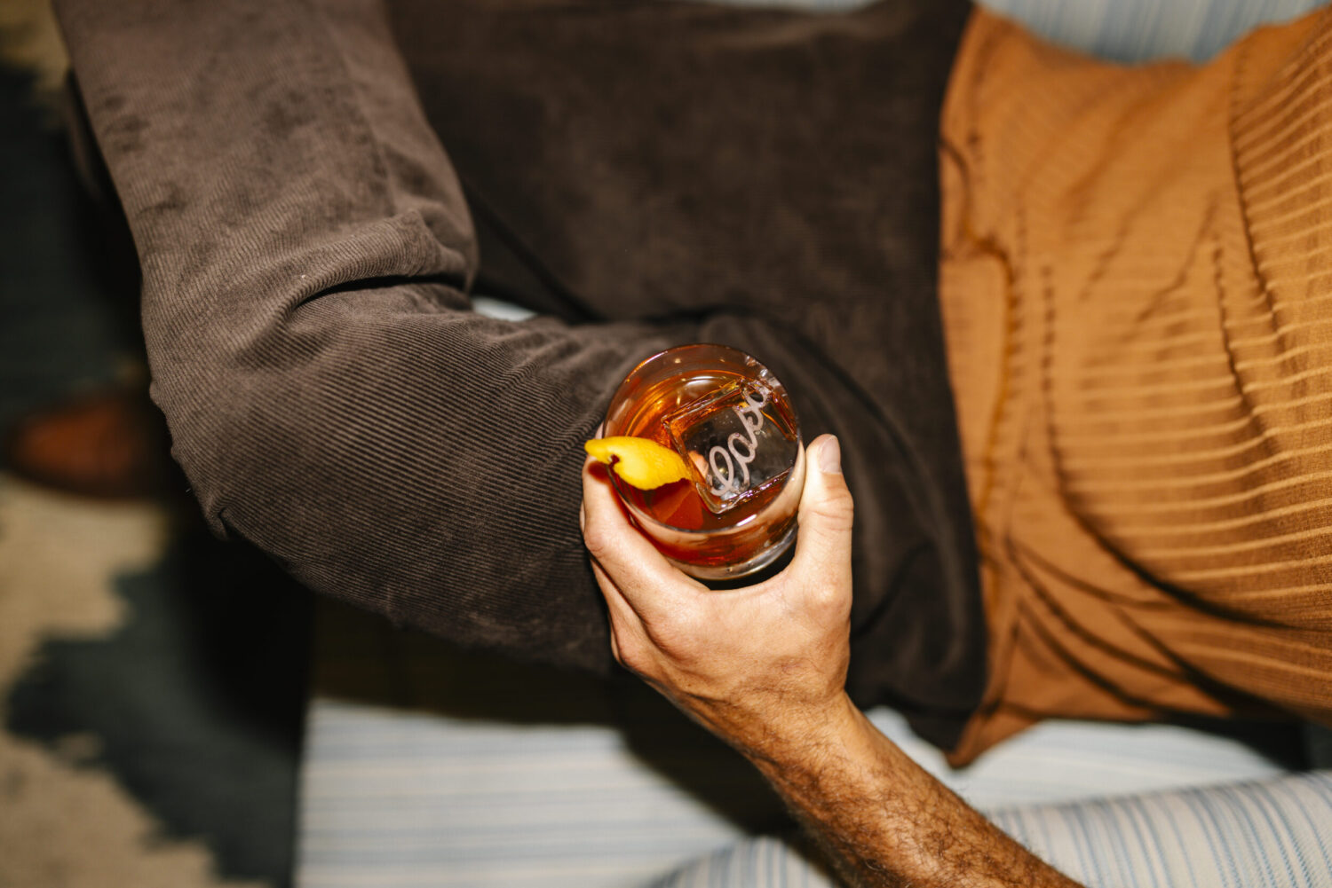 Hand holding a cocktail glass garnished with an orange twist, with 'Casa' engraved in the ice.