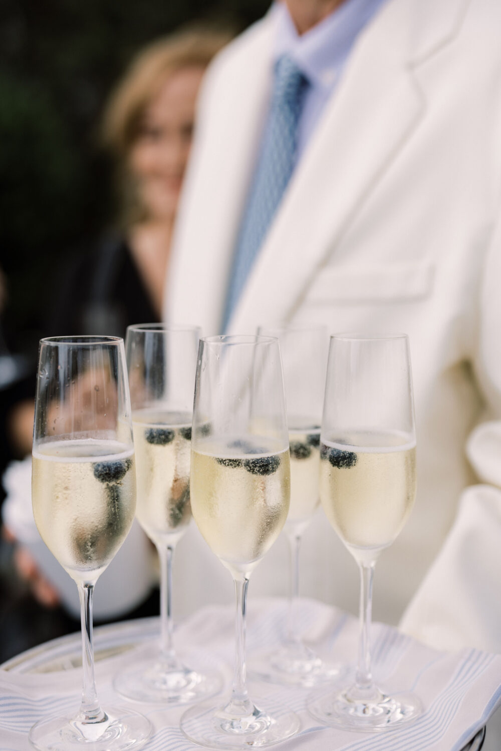 a server holding 5 glasses of champagne, at a party