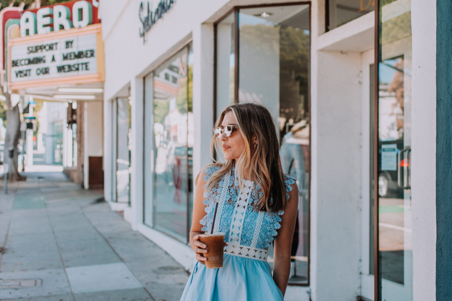 woman with iced latte standing by the shop windows
