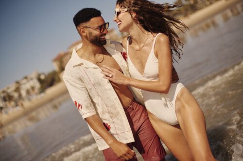 man and a woman laughing and facing each other, walking in the ocean