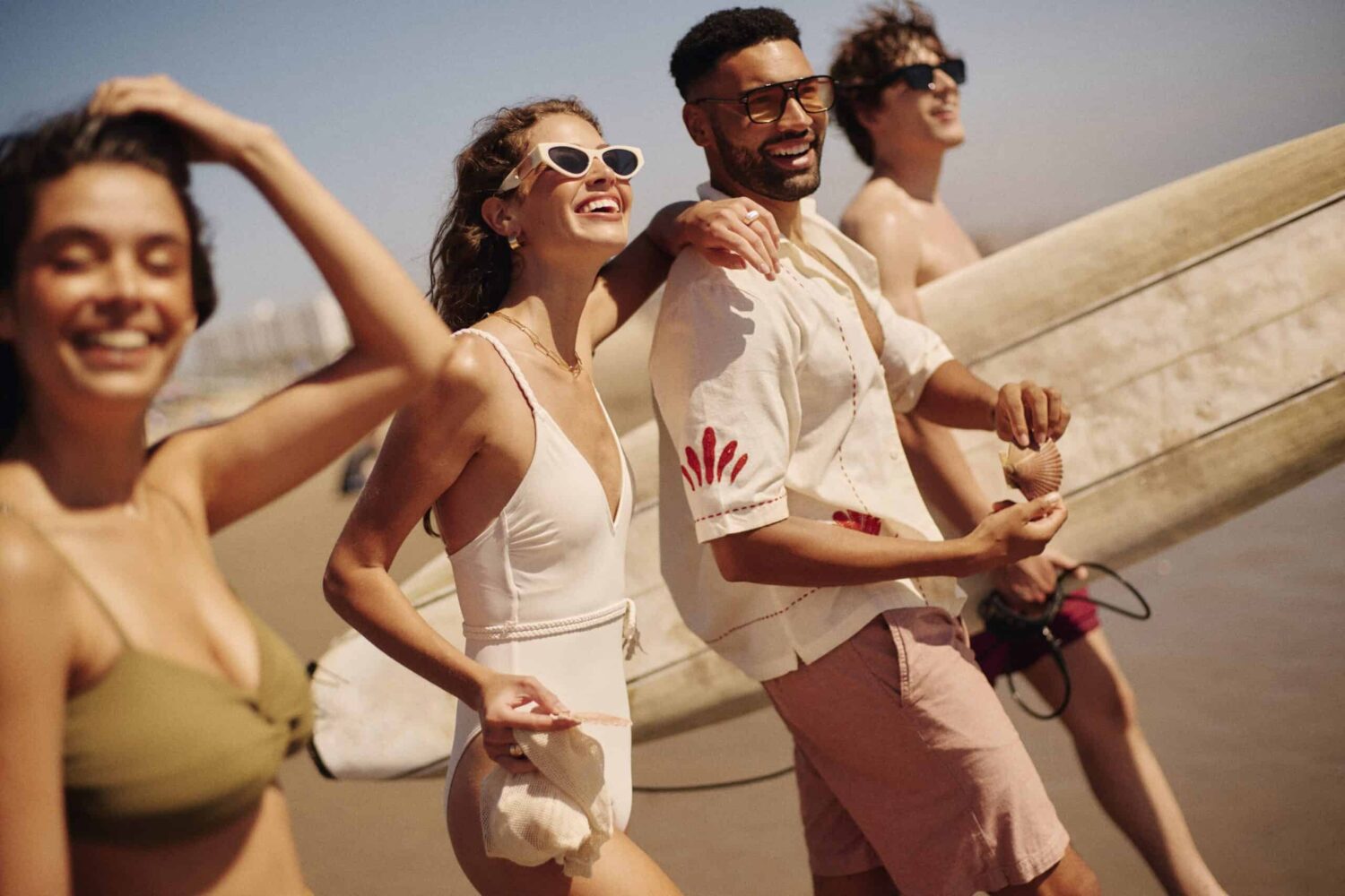 Close-up of four friends on the beach, one with a seashell, another with a surfboard.