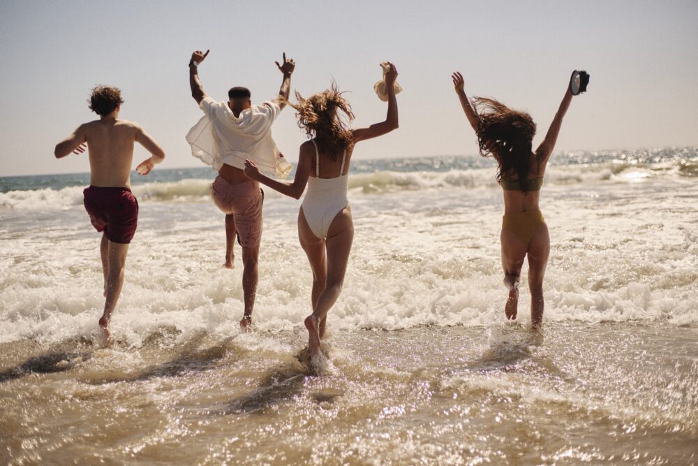four friends in swimsuits running into the ocean with their hands in the air