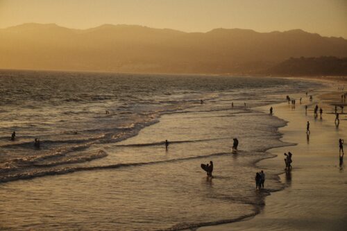 a sunset shot, from above, of the beach waves and human silhouettes