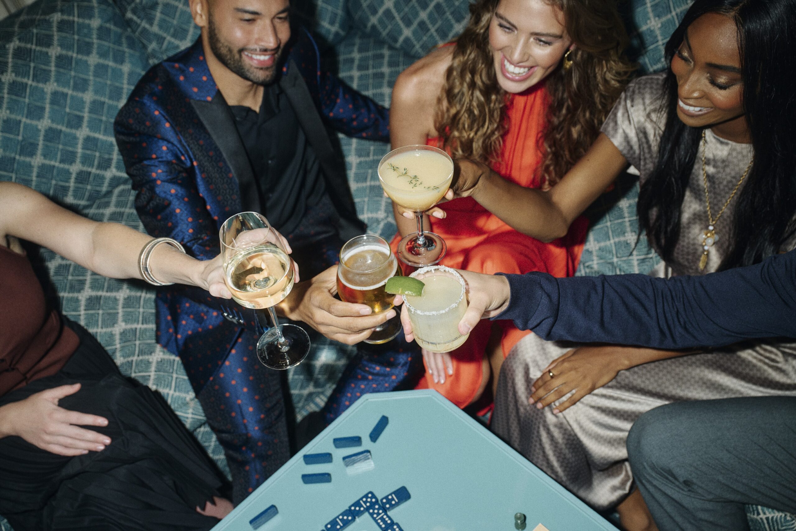 a shot from above of four friends clinking their cocktails to cheers, on the couch at the hotel bar