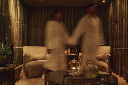 A man and woman in robes walk out of the frame in the hotel spa's sitting room, out of focus.