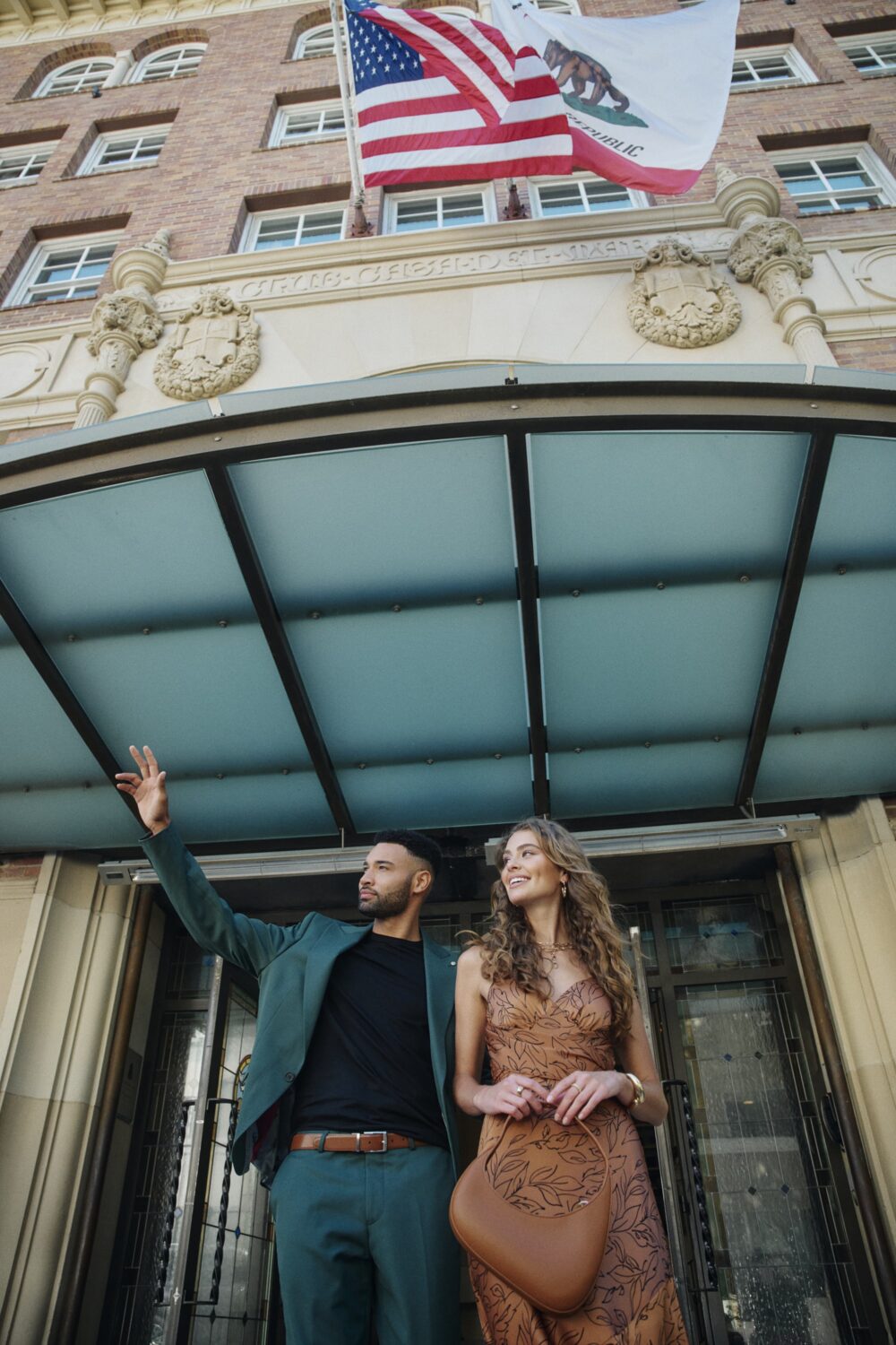 Close-up from below of a man and woman exiting the luxury hotel under the flags.