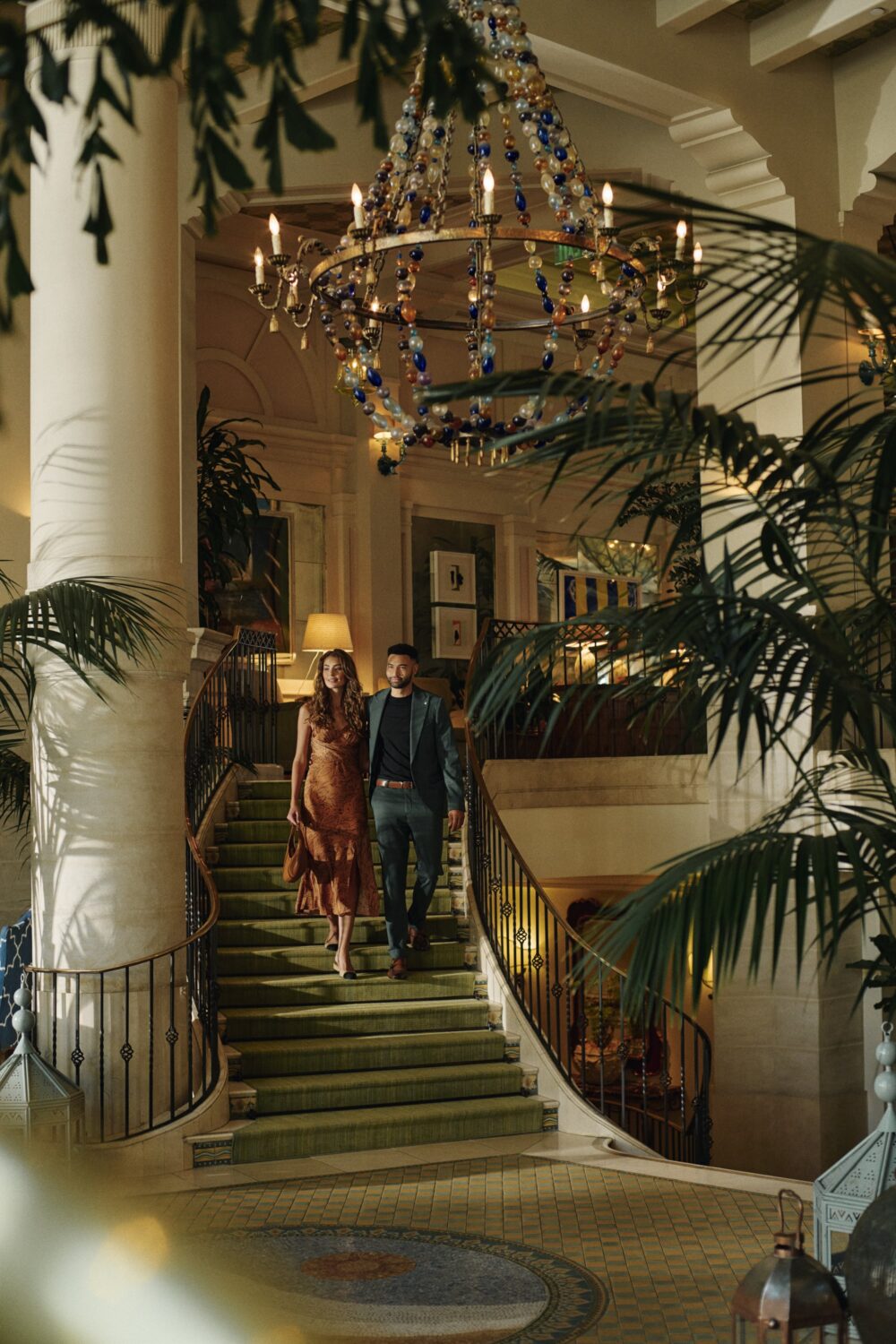 A man and a woman walking down the lobby stairs, dressed for dinner, with a mosaic tiled floor