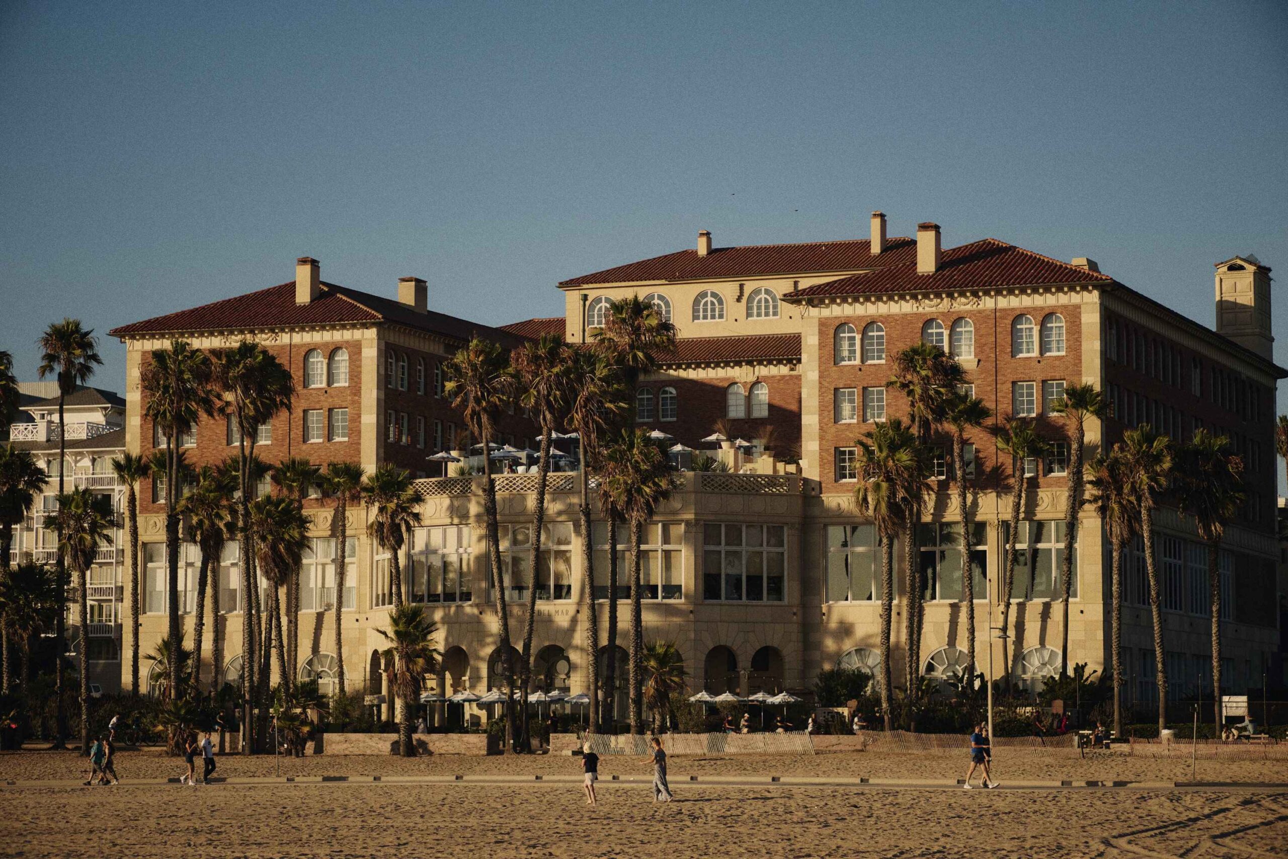 Exterior shot of Casa del Mar Hotel taken from the beach, displaying palm trees and humans walking