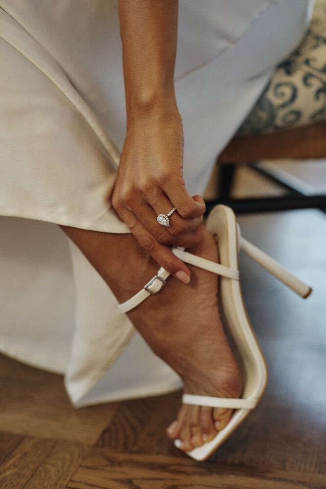 close up shot of a woman's foot and hand, on her wedding day, displaying her ring and shoes
