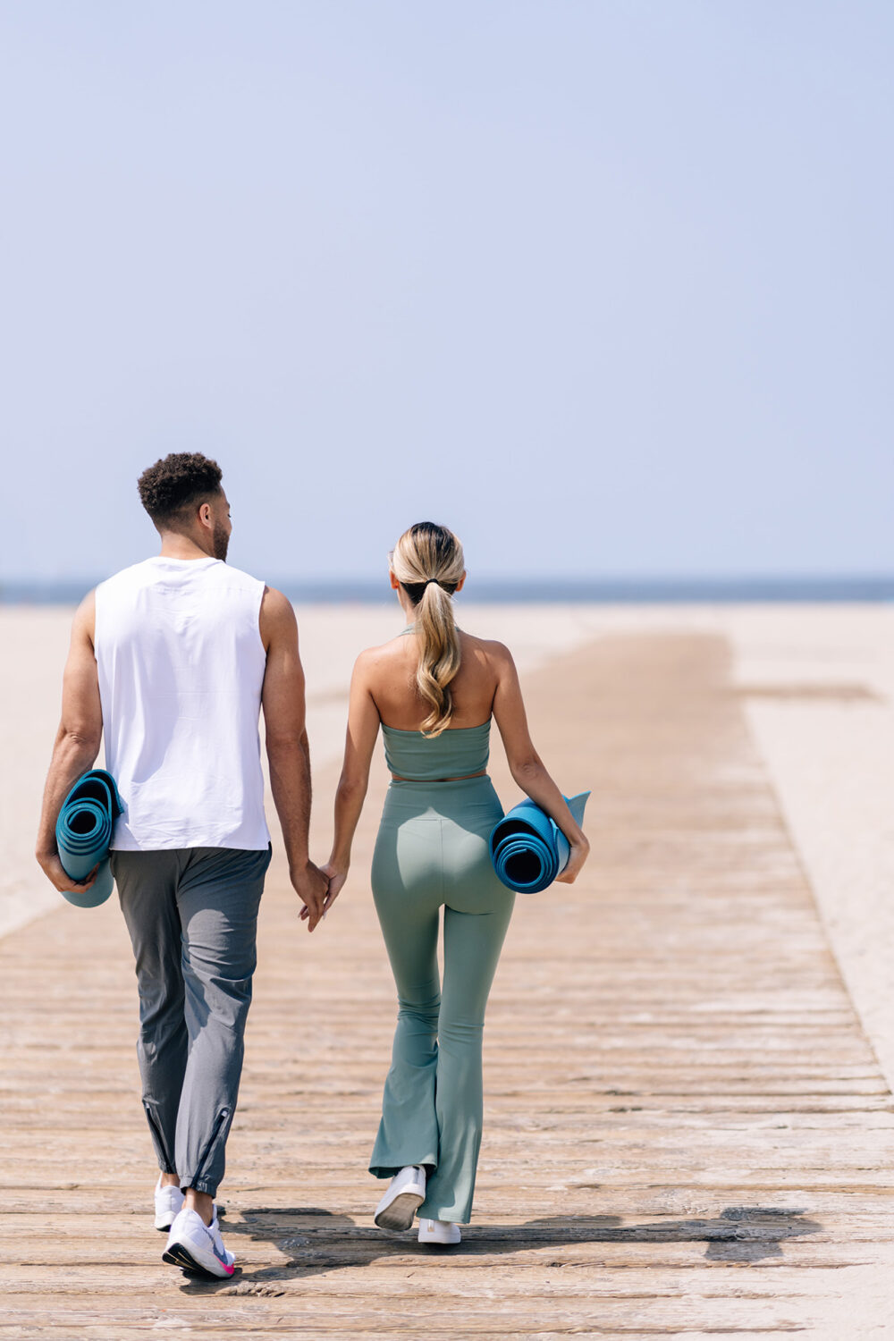 man and woman, holding yoga mats walking to the beach