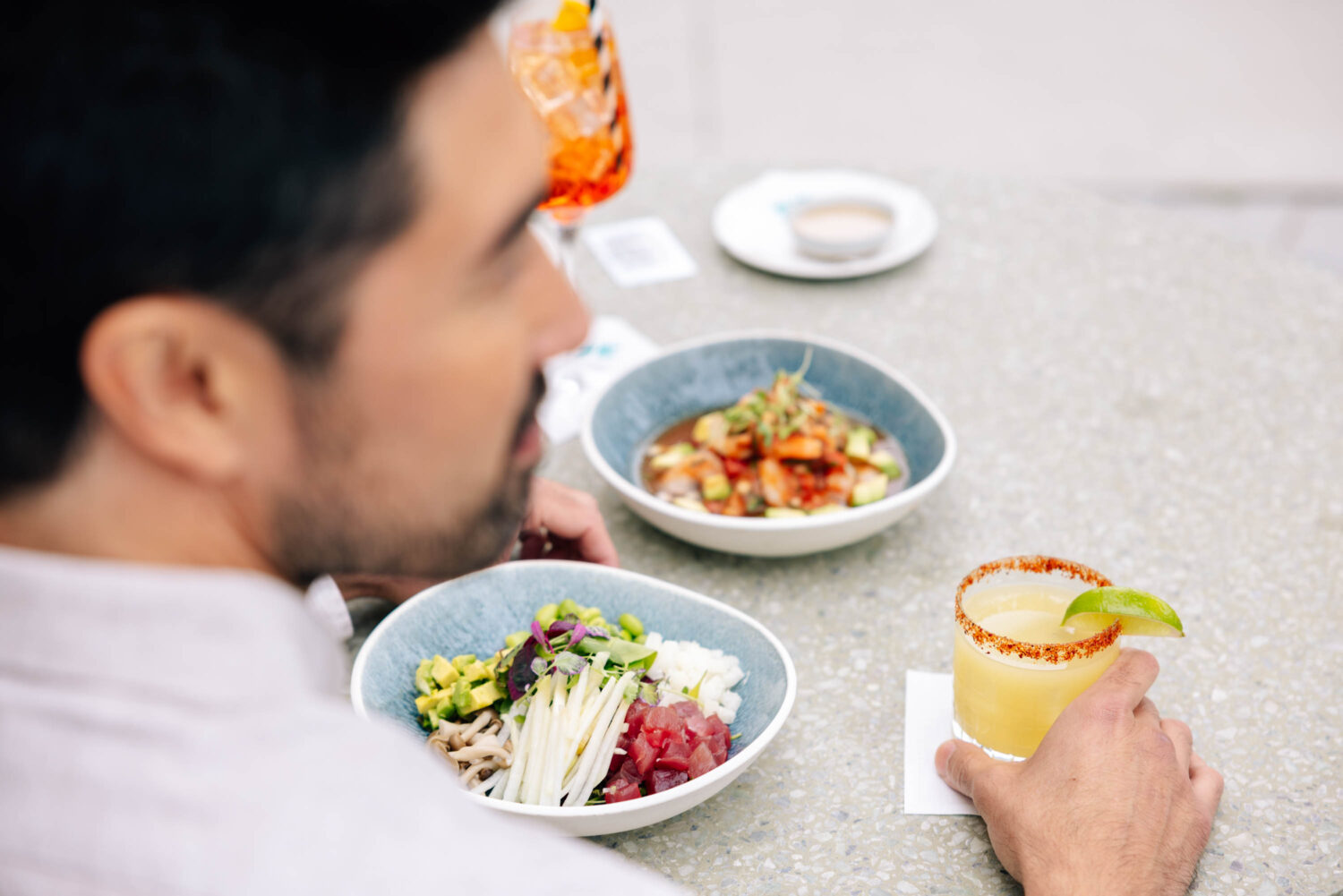 man at the table holding a frozen margarita with 2 food dishes