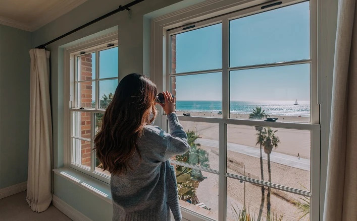 woman looking out the window with binoculars at the beach